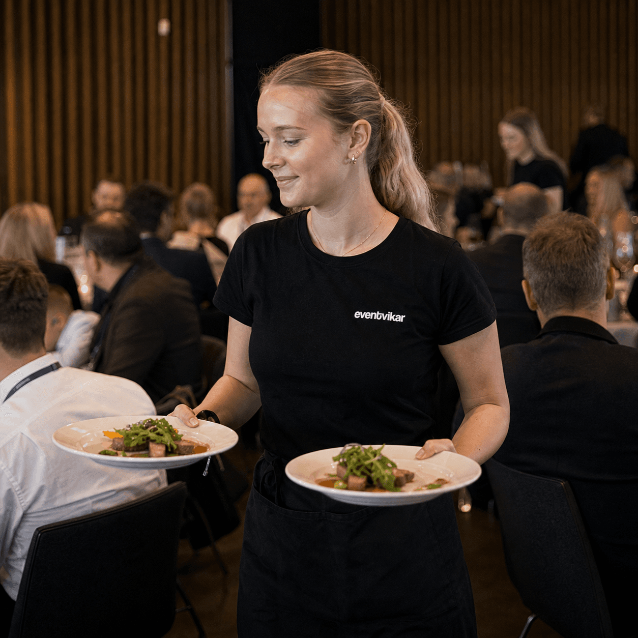 Eventvikar serveringspersonale bærer tallerkener gennem et event